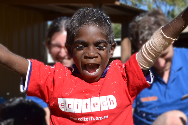 An indigenous child in a red scitech shirt has his arms up and is cheering