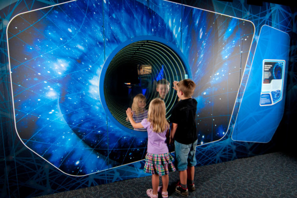 Two young children playing infront of a worm hole simulator in the Science Fiction Science Future Exhibition.